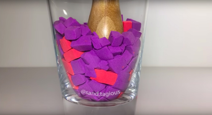 Very Satisfying Video Compilation 80 Kinetic Sand Cutting ASMR." Blocks of red and purple sand in a jar being tamped down by a wooden pickle packer.